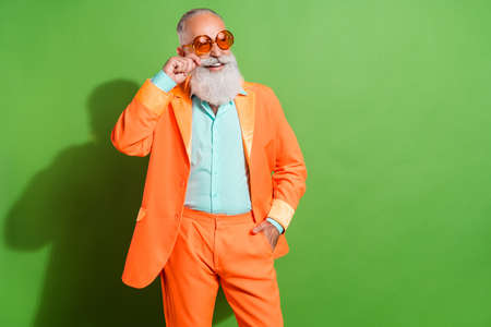 Portrait of attractive cheerful grey-haired man posing touching mustache copy space isolated over bright green color backgroundの写真素材