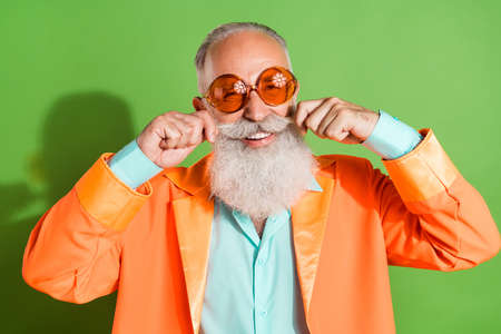 Portrait of attractive cheerful man wearing specs touching mustache good look isolated over bright green color backgroundの写真素材
