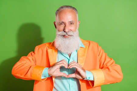 Portrait of attractive cheerful grey-haired man showing heart symbol isolated over bright green color backgroundの写真素材