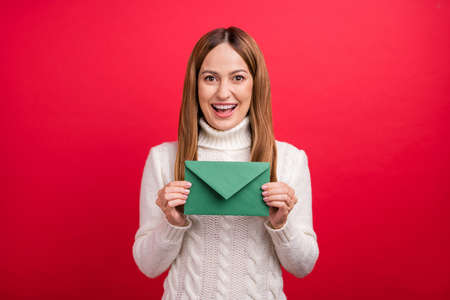 Portrait of attractive cheerful woman holding in hands letter list postal isolated over bright red color backgroundの写真素材