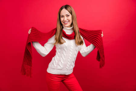 Portrait of attractive cheerful woman showing wearing warm scarf posing isolated over bright red color backgroundの写真素材