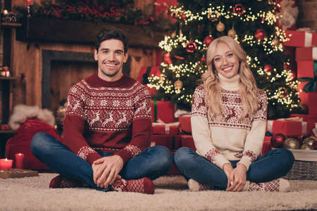 Photo of dreamy attractive young wife husband wear print sweaters smiling enjoying noel time sitting legs crossed indoors house home roomの写真素材