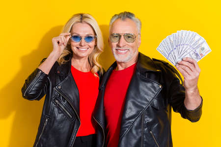 Portrait of pensioner beautiful handsome cheerful spouses holding cashback credit bank isolated over bright yellow color backgroundの写真素材