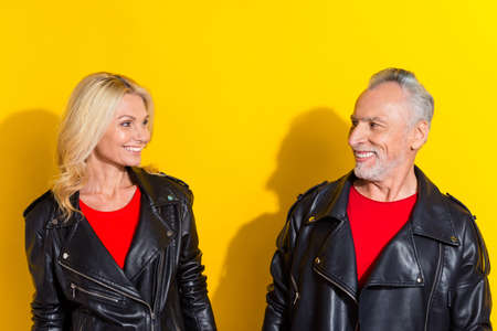 Portrait of two attractive cheerful cool grey-haired spouses looking at each other isolated over bright yellow color backgroundの写真素材