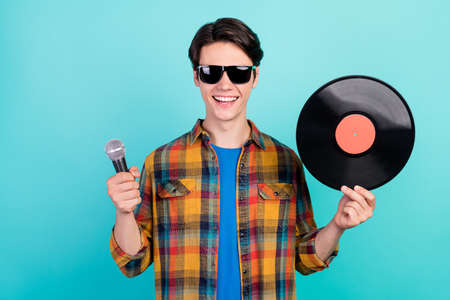 Photo of cheerful dj guy hold mic hand vinyl disk wear sunglass plaid shirt isolated aquamarine color backgroundの写真素材