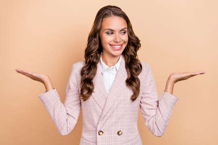 Photo of cheerful pretty lady look interested hands demonstrate empty space solution isolated on beige color backgroundの写真素材