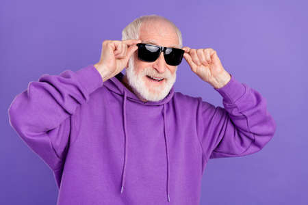 Portrait of attractive cheerful grey-haired man touching specs good mood isolated over bright violet purple color backgroundの写真素材