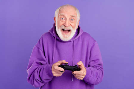 Portrait of attractive cheery addicted grey-haired man playing game having fun isolated over bright violet purple color backgroundの写真素材