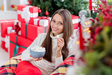 Photo of attractive adorable young woman dressed white sweater eating christmas snacks smiling indoors house home roomの写真素材