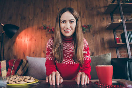 Photo of funny cheerful young woman dressed red sweater typing modern gadget new year wishes smiling indoors room home houseの写真素材