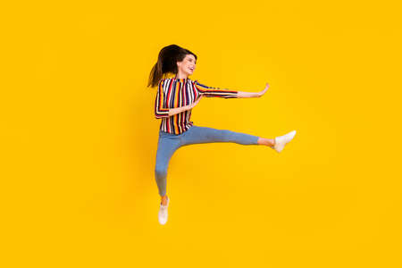 Full length body size photo girl in casual clothes jumping practising martial arts isolated bright yellow color backgroundの写真素材