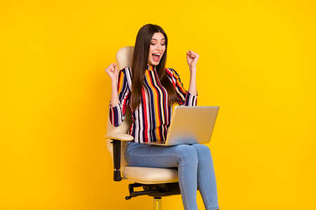 Profile side photo of young woman happy positive smile sit stool look laptop rejoice victory isolated over yellow color backgroundの写真素材