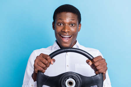 Photo of funny impressed dark skin man wear white shirt smiling holding steering wheel isolated blue color backgroundの写真素材