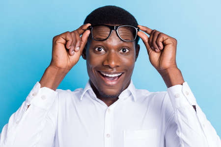 Photo of excited funny dark skin guy dressed formal shirt arms glasses big eyes open mouth isolated blue color backgroundの写真素材