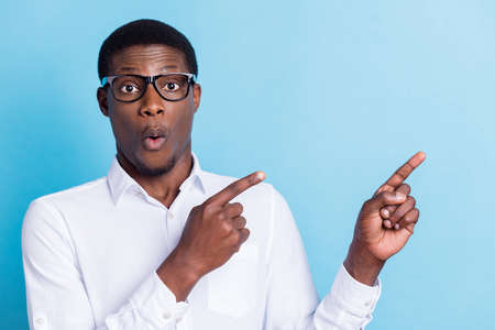 Photo of impressed shocked dark skin man wear white shirt spectacles pointing empty space isolated...