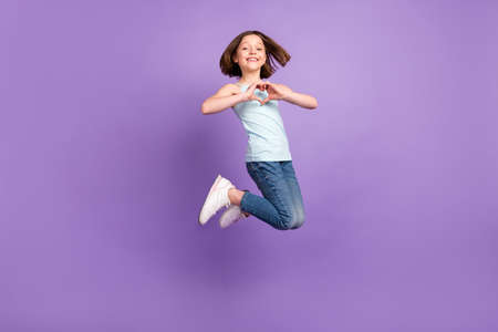Full size photo of cheerful happy lovely little girl jump up good mood make heart fingers isolated on violet color backgroundの写真素材