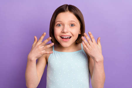 Photo of funky brown hairdo small girl hands up wear blue top isolated on violet color backgroundの写真素材