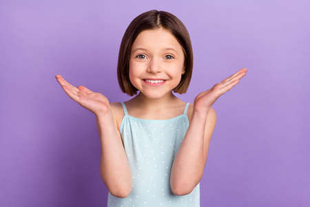 Photo of charming little happy girl hold hands empty space smile good mood isolated on purple color backgroundの写真素材