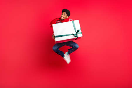Full length photo of young afro guy happy positive smile jump gift holiday spirit new year isolated over red color backgroundの写真素材