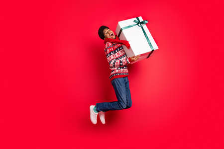 Full body profile side photo of young afro guy happy smile jump hold present box christmas isolated over red color backgroundの写真素材