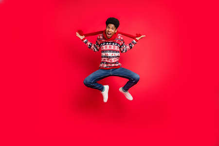 Full body photo of young afro guy happy positive smile jump up scarf winter holiday isolated over red color backgroundの写真素材