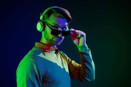 Photo of young cool millennial guy wear headphones spectacles sweater isolated on dark blue color backgroundの写真素材