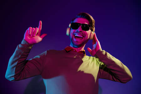 Photo of young cool dj guy wear headphones spectacles sweater isolated on dark blue color backgroundの写真素材