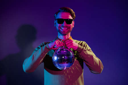 Photo portrait young man in sunglass smiling keeping disco ball isolated gradient violet color backgroundの写真素材