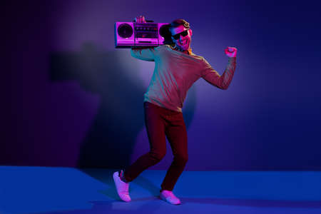 Full length photo of cheerful young man raise fist winner dance hold boombox isolated on neon backgroundの写真素材