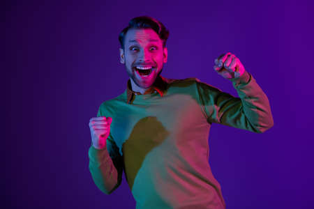Photo of amazed young shocked excited man winner raise fists good mood isolated on violet neon color backgroundの写真素材