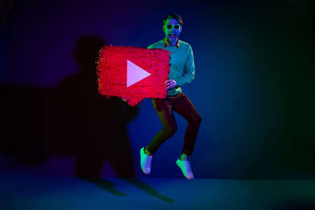 Full length body size photo man in sunglass jumping with streaming service icon isolated on dark blue color backgroundの写真素材