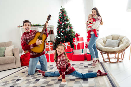 Full body photo of wife husband people childhood parents children xmas play guitar christmas tree indoors inside house homeの写真素材