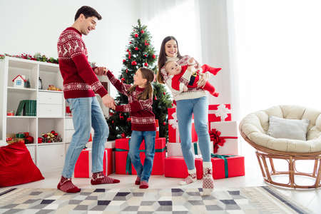 Photo of funky cheerful couple two kids dressed new year pullovers smiling holding arms hands dancing indoors house home roomの写真素材