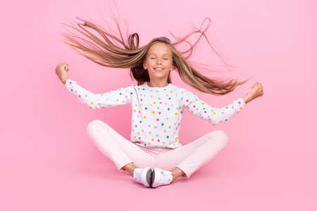 Photo of peaceful serene little lady sit floor meditate throw hair wear dotted shirt isolated pink color backgroundの写真素材
