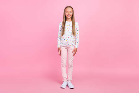 Photo of cheerful positive candid little lady look camera wear dotted shirt pants shoes isolated pink color backgroundの写真素材