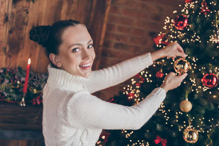 Photo of funny sweet young woman dressed knitted sweater decorating new year tree smiling indoors room home houseの写真素材