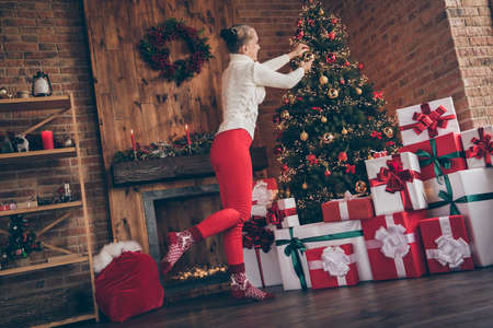 Photo of shiny pretty young woman dressed knitted sweater decorating new year tree smiling indoors room home houseの写真素材