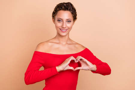 Photo of romantic happy pretty young lady make heart figure celebrate spring holiday isolated on pastel beige color backgroundの写真素材