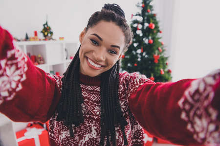Self-portrait of attractive cheerful trendy girl spending day festal time vacation weekend ugly pullover at decorated home indoorsの写真素材