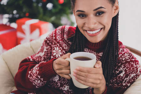 Cropped view portrait of attractive cheerful girl sitting in cosy chair drinking beverage ugly...