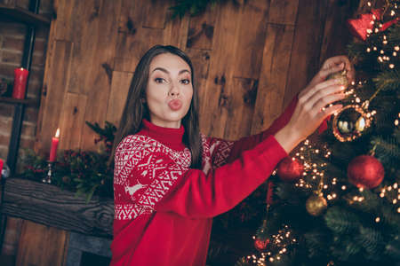 Photo of beautiful attractive young woman dressed red sweater decorating new year tree sending kiss indoors room home houseの写真素材