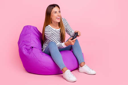 Full length photo of young brown hairdo lady sit playstation wear shirt jeans shoes isolated on pink...