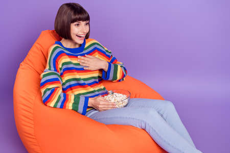 Photo of funny lady sit beanbag hold popcorn watch comedy laugh wear striped sweater isolated violet...