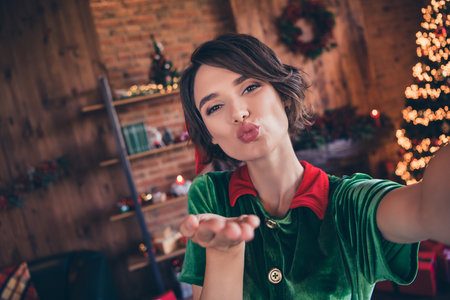 Self-portrait of attractive cheerful girl elf sending you air kiss staying at home modern loft...