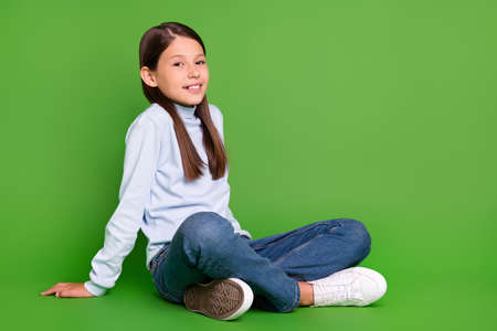 Photo of charming cute school girl dressed blue turtleneck sitting floor empty space smiling isolated green color backgroundの写真素材