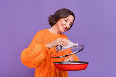 Profile side photo of cheerful elderly woman cooking delicious dish recipe check isolated over purple color backgroundの写真素材