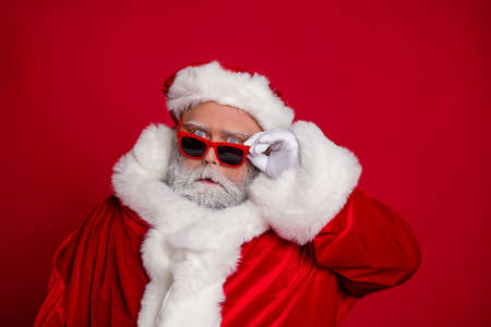 Portrait of attractive funny comic moody amazed stunned Santa touching specs isolated over vibrant red color backgroundの写真素材