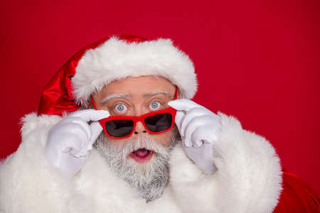 Photo of excited shocked old man take off specs sale omg reaction wear santa hat costume isolated red color backgroundの写真素材