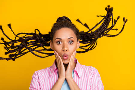 Photo of young amazed afro american shocked woman hold hands cheeks hair fly isolated on yellow color backgroundの写真素材