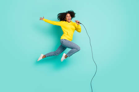 Full length body size photo woman jumping up singing in microphone isolated bright teal color backgroundの写真素材